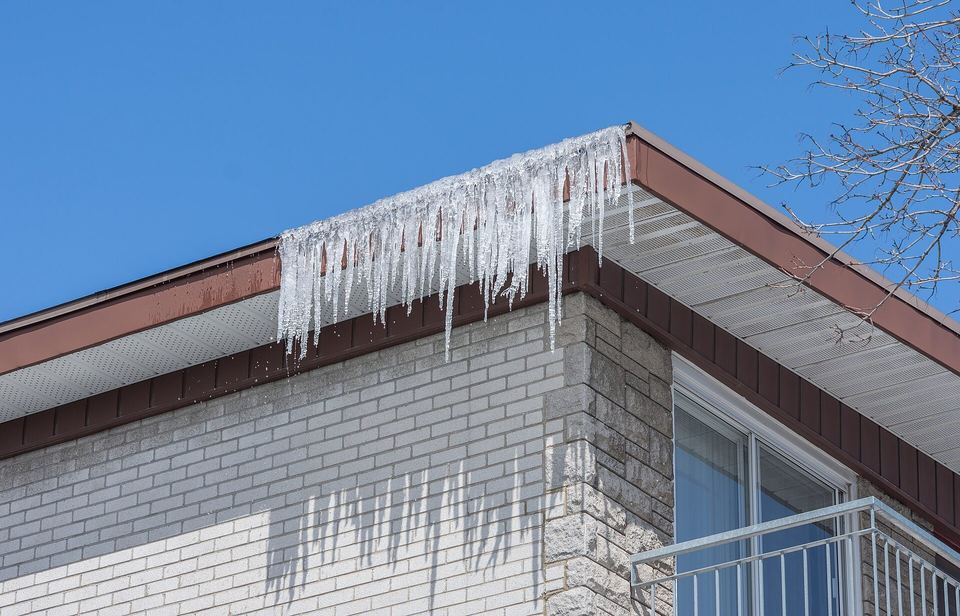 Long icicles hanging from the eaves and soffit at the corner of a house
