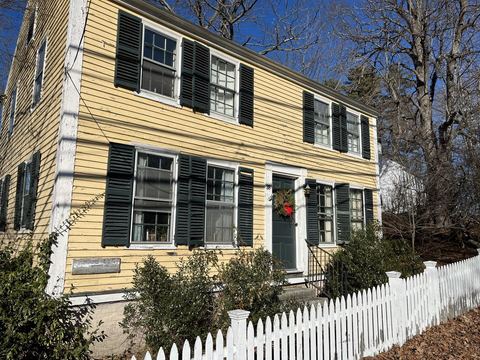Yellow clapboard house with black shutters behind a white picket fence
