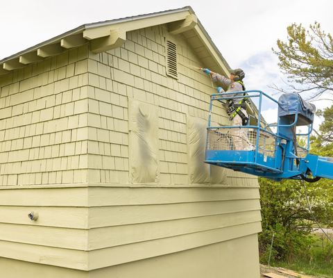 Worker on a lift painting new shingle and lap siding on a house gable